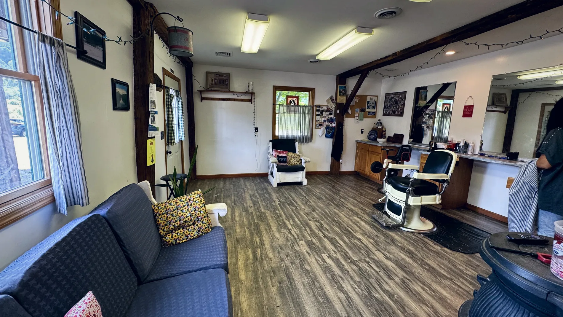 The whole shop room — the waiting couch, hand-hewn beams, string lights, and the antique barber chair by the mirrors.
