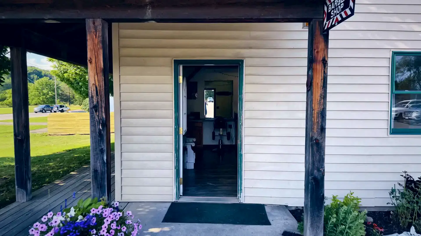 The open green front door of Doris's Barber Shop, seen from the porch.